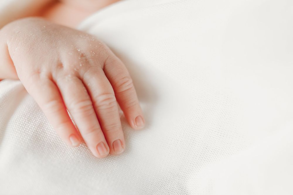 Close-up of tiny baby hands resting on white fabric.