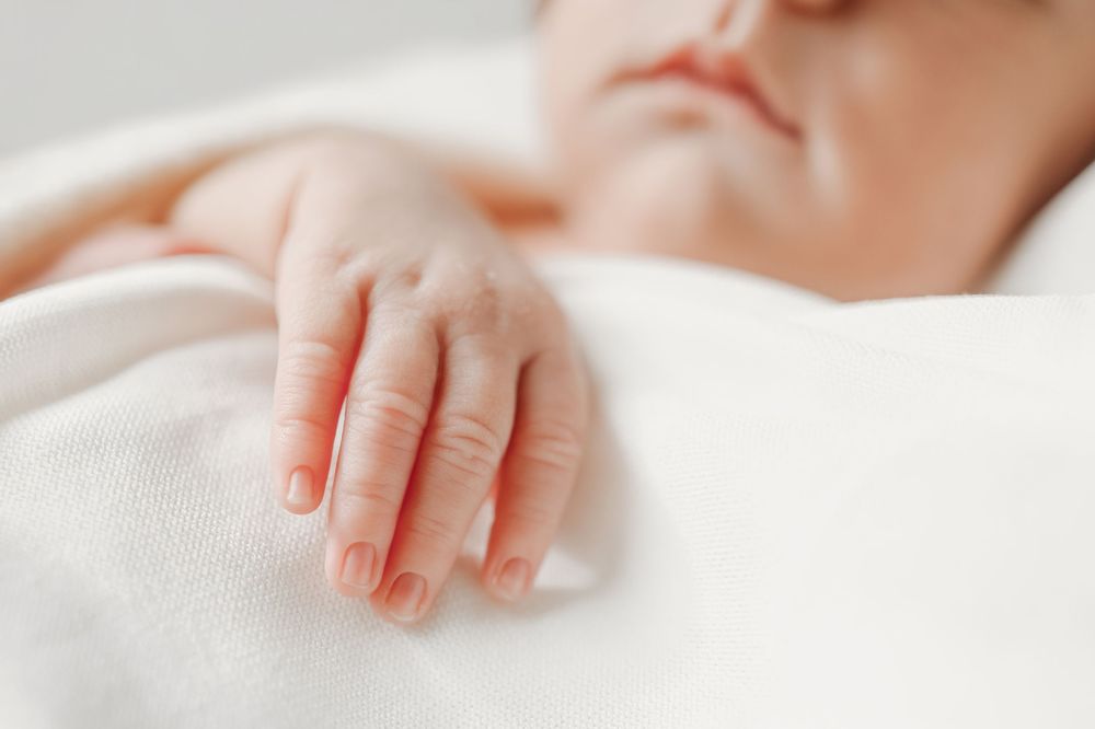 Small infant hands gently touching white textured fabric.