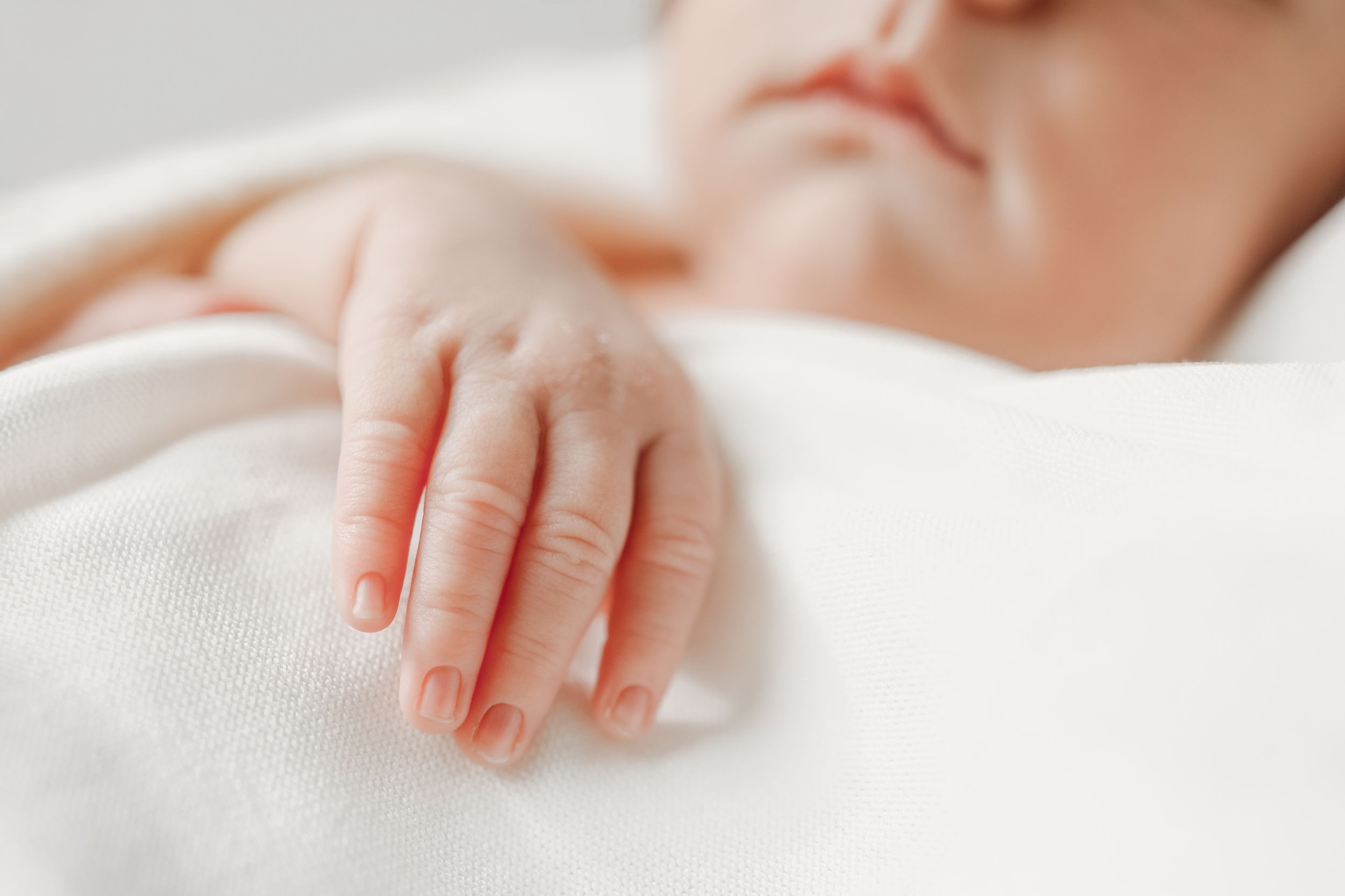 Small infant hands gently touching white textured fabric.