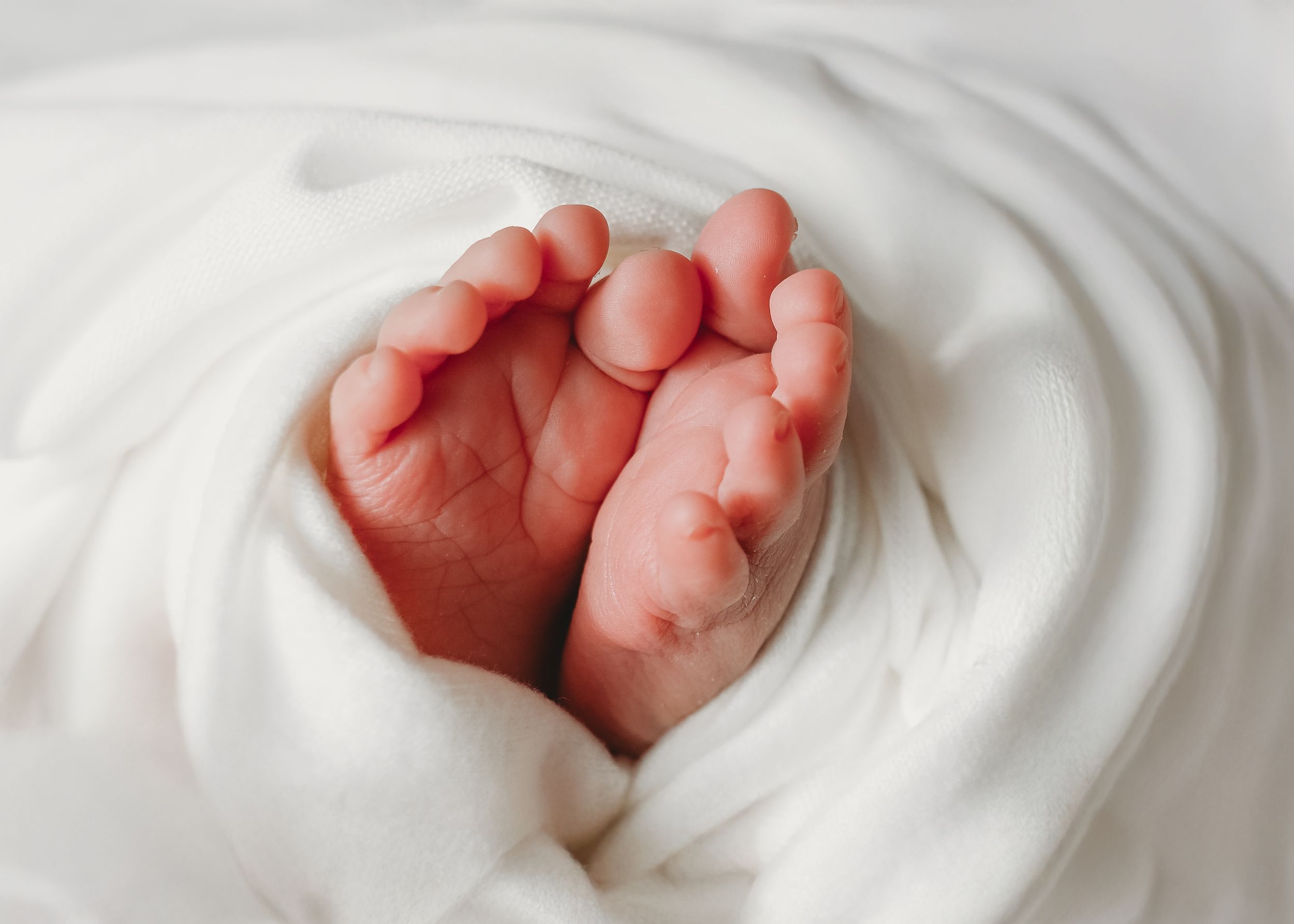 Delicate baby feet peeking out from white blanket.
