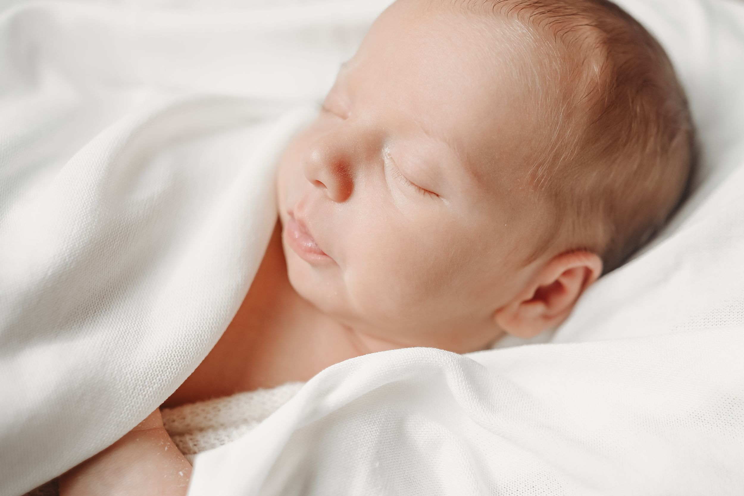 Peaceful newborn resting on soft white linens.