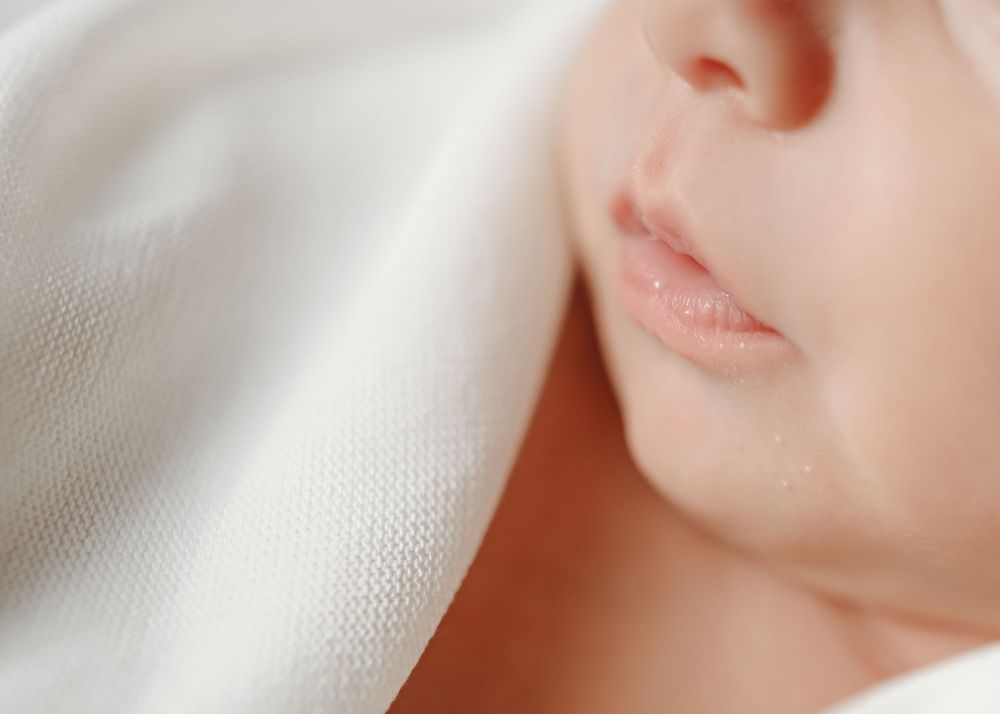 Gentle profile view of sleeping baby against white fabric.