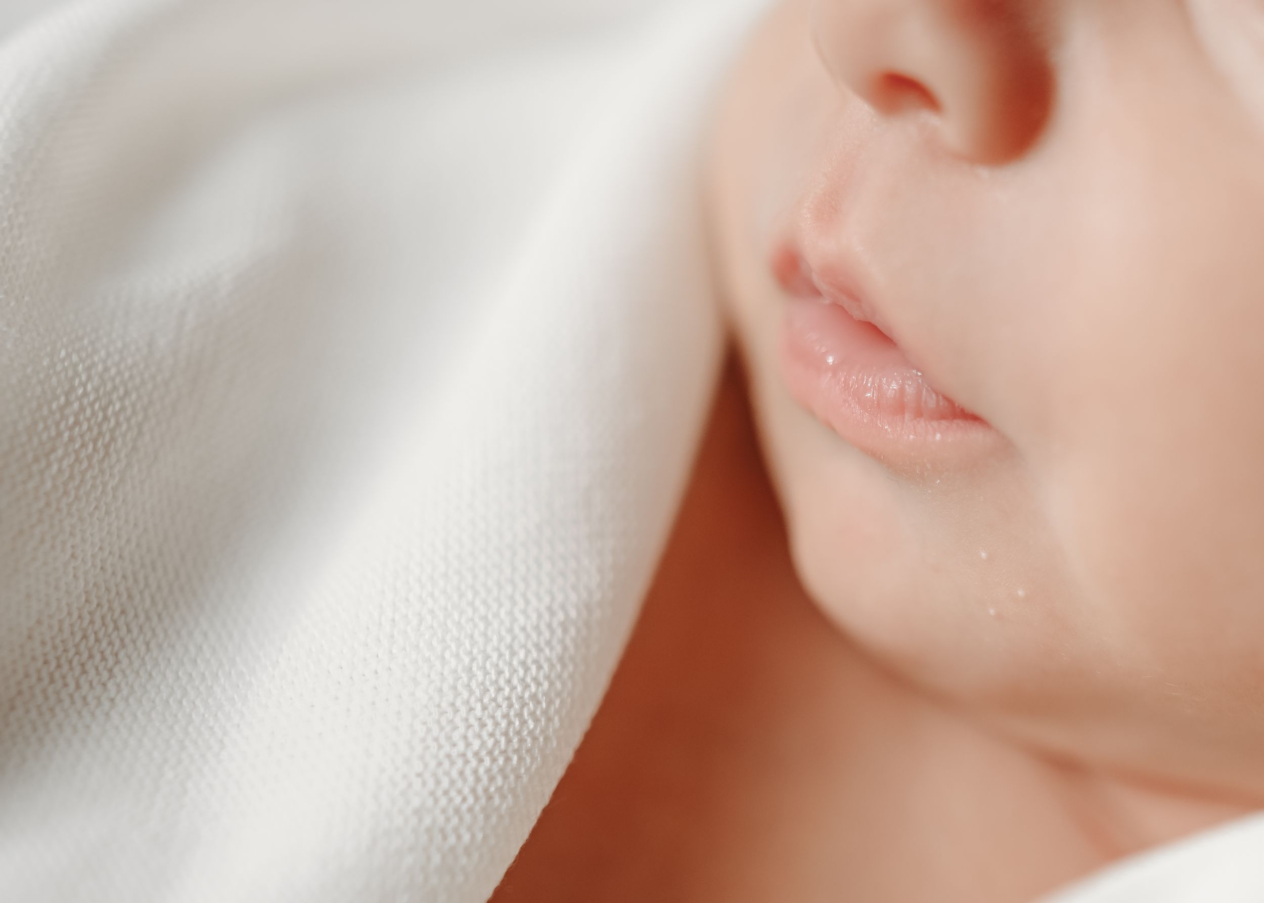 Gentle profile view of sleeping baby against white fabric.