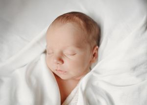 Newborn sleeping peacefully wrapped in white fabric.