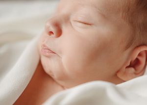 Soft profile view of sleeping baby against white background.