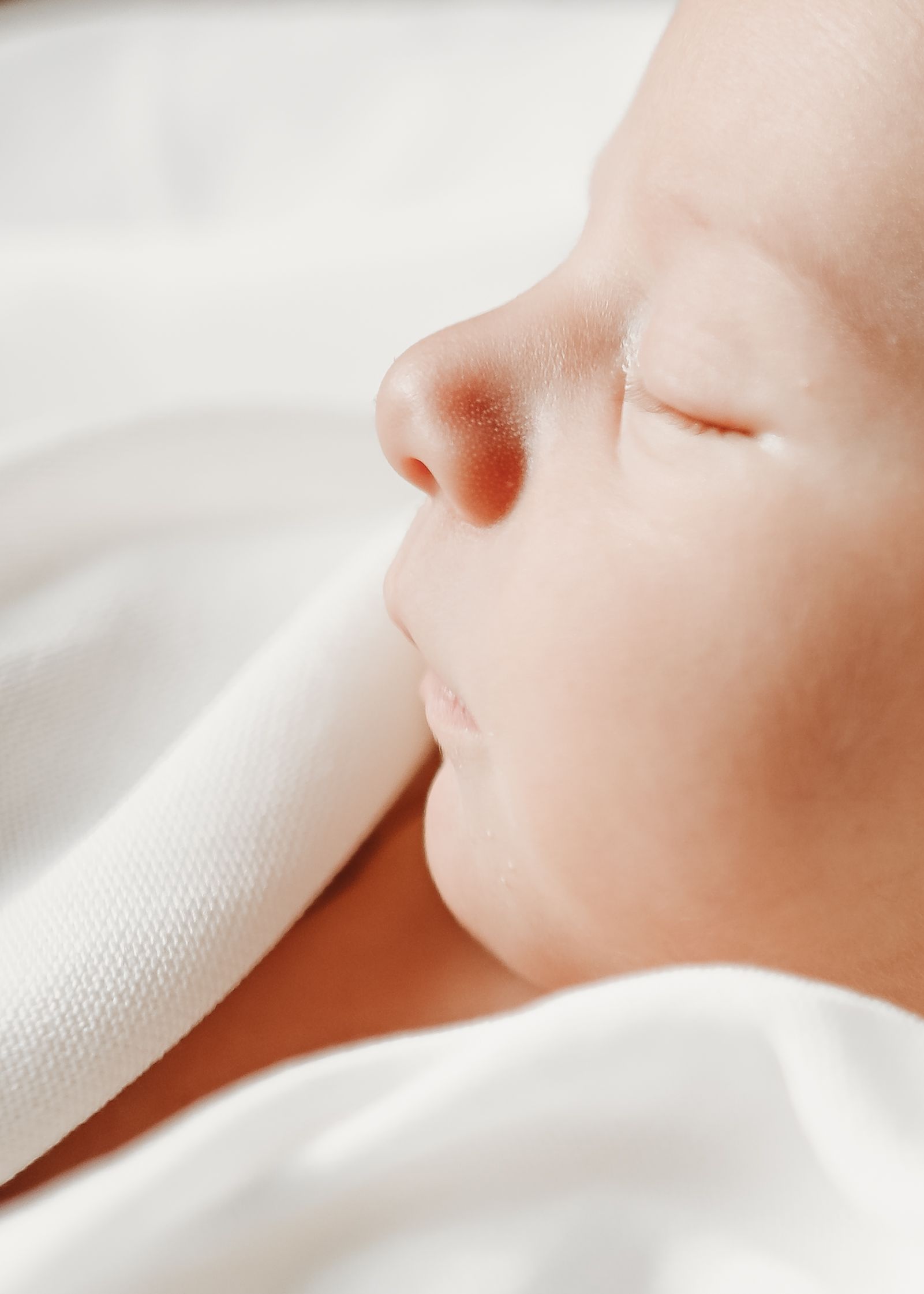 Delicate close-up of a baby's skin and nose against soft white fabric, showcasing gentle texture and natural lighting.