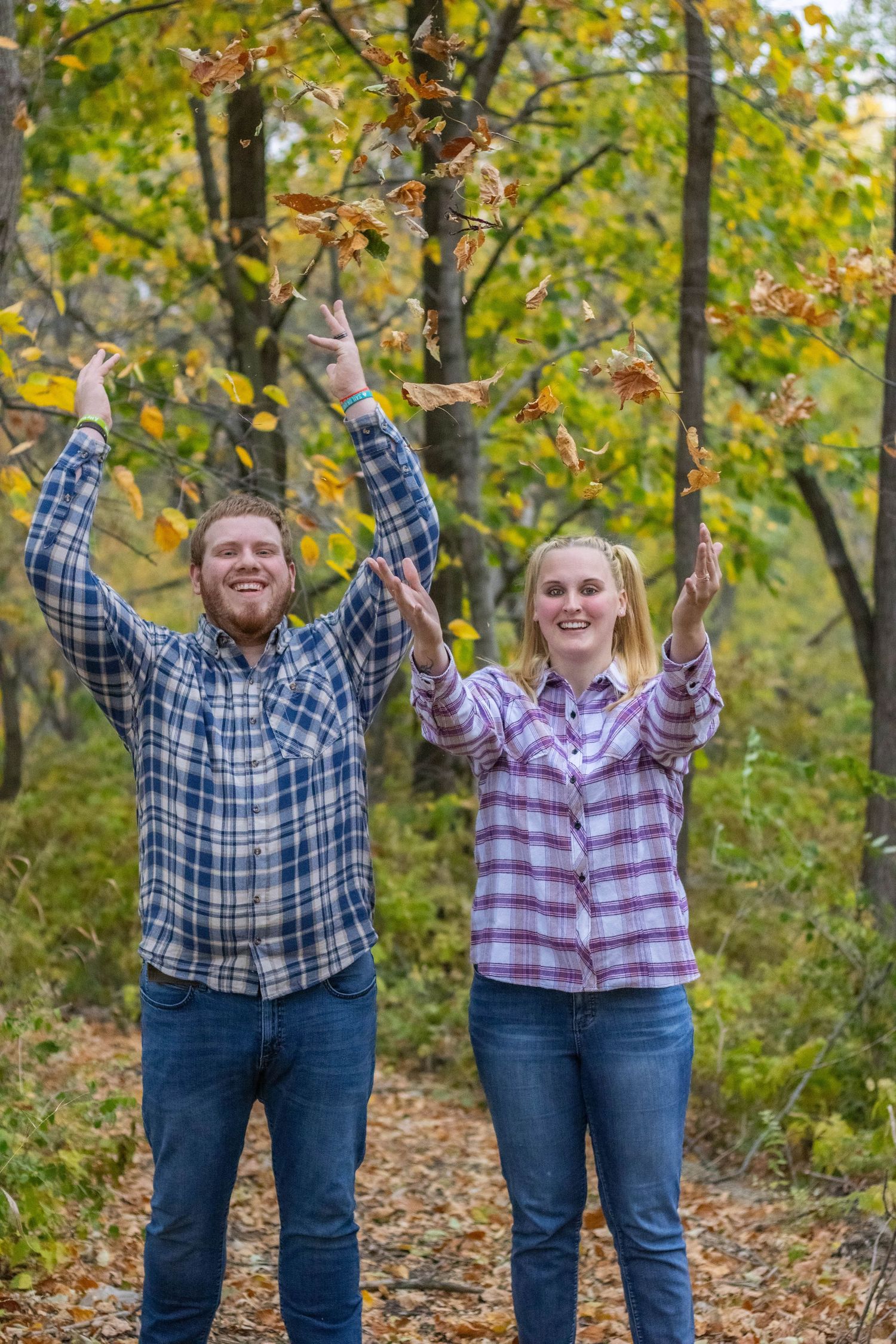 Couple in plaid shirts throws autumn leaves in the air while enjoying nature.