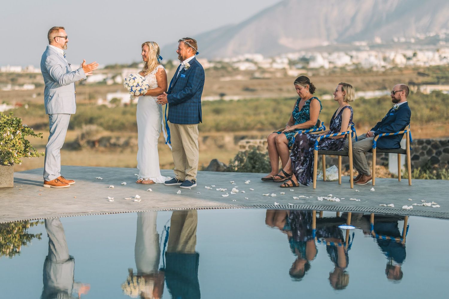 Wedding ceremony by infinity pool with mountain backdrop and guests seated.