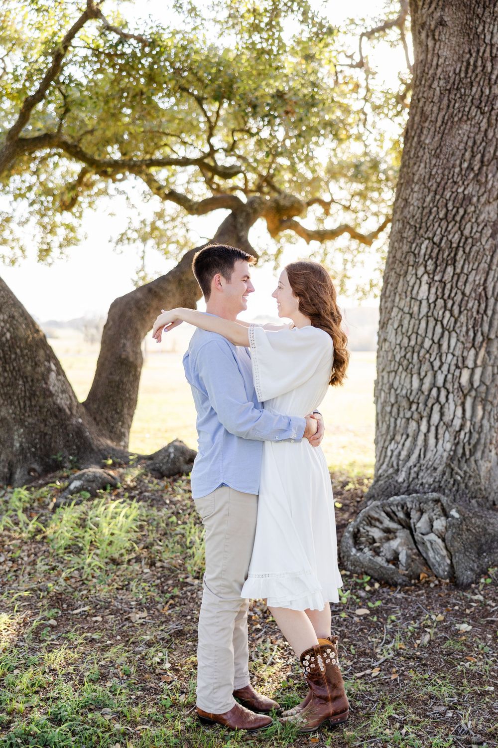 A romantic couple embraces by a majestic oak tree on a sunny afternoon.