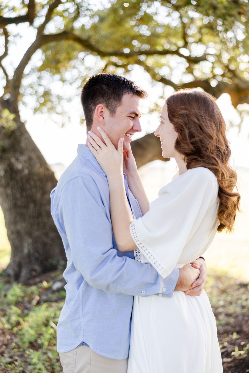 A couple embraces intimately beneath a large tree with golden sunlight streaming through the branches.
