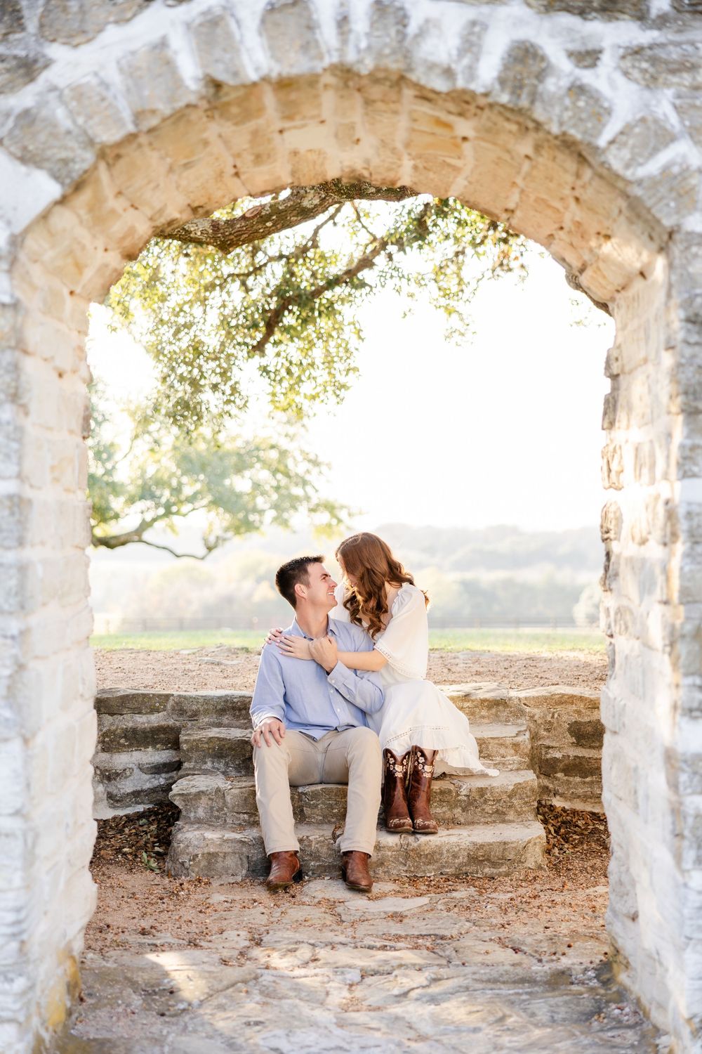 A romantic scene under a stone archway as a couple share an intimate moment on rustic steps at sunset.