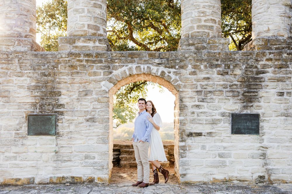 A couple poses in a romantic stone archway of historic ruins with soft natural lighting.
