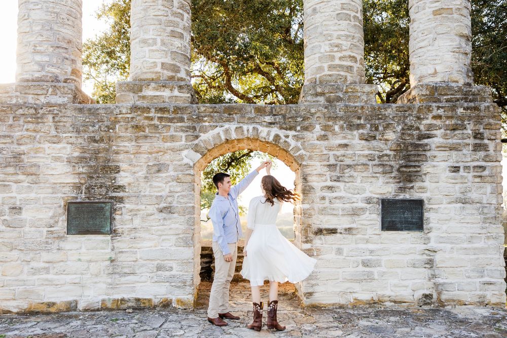 A couple dances playfully in a stone archway of ancient ruins during their engagement photoshoot.