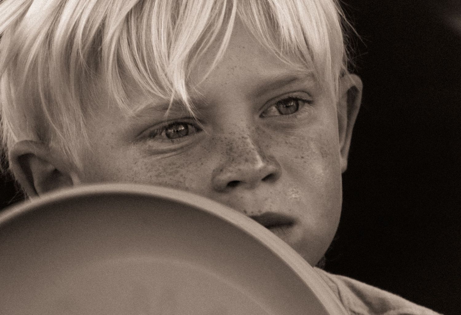 Young boy with a frisbee toy up to his freckled face in Florida. Black and White photography.