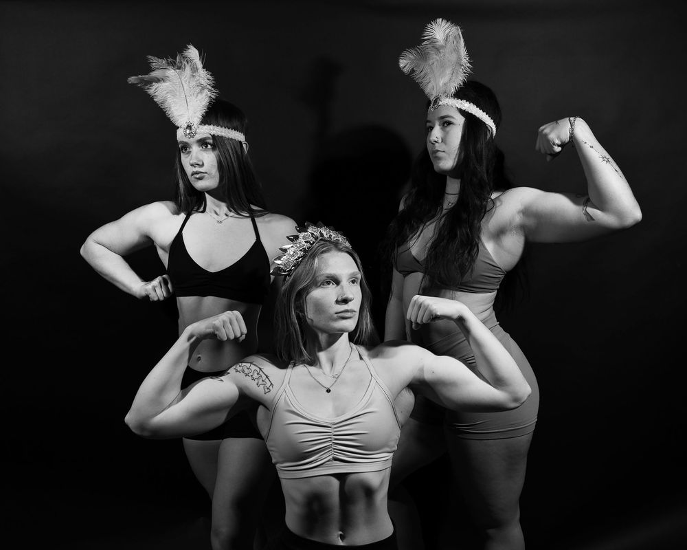 A black and white portrait of three muscular women with headpieces on