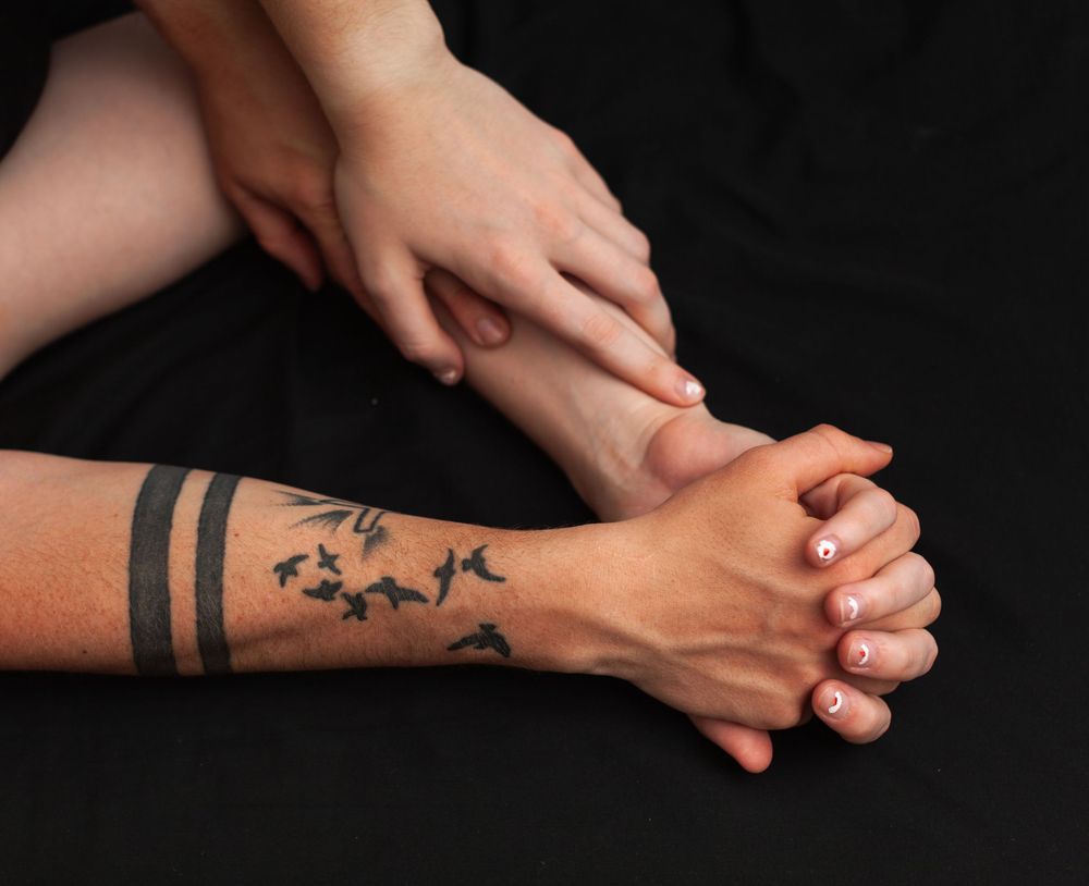 Two people holding hands, one of the hands has tattoos of birds and black lines