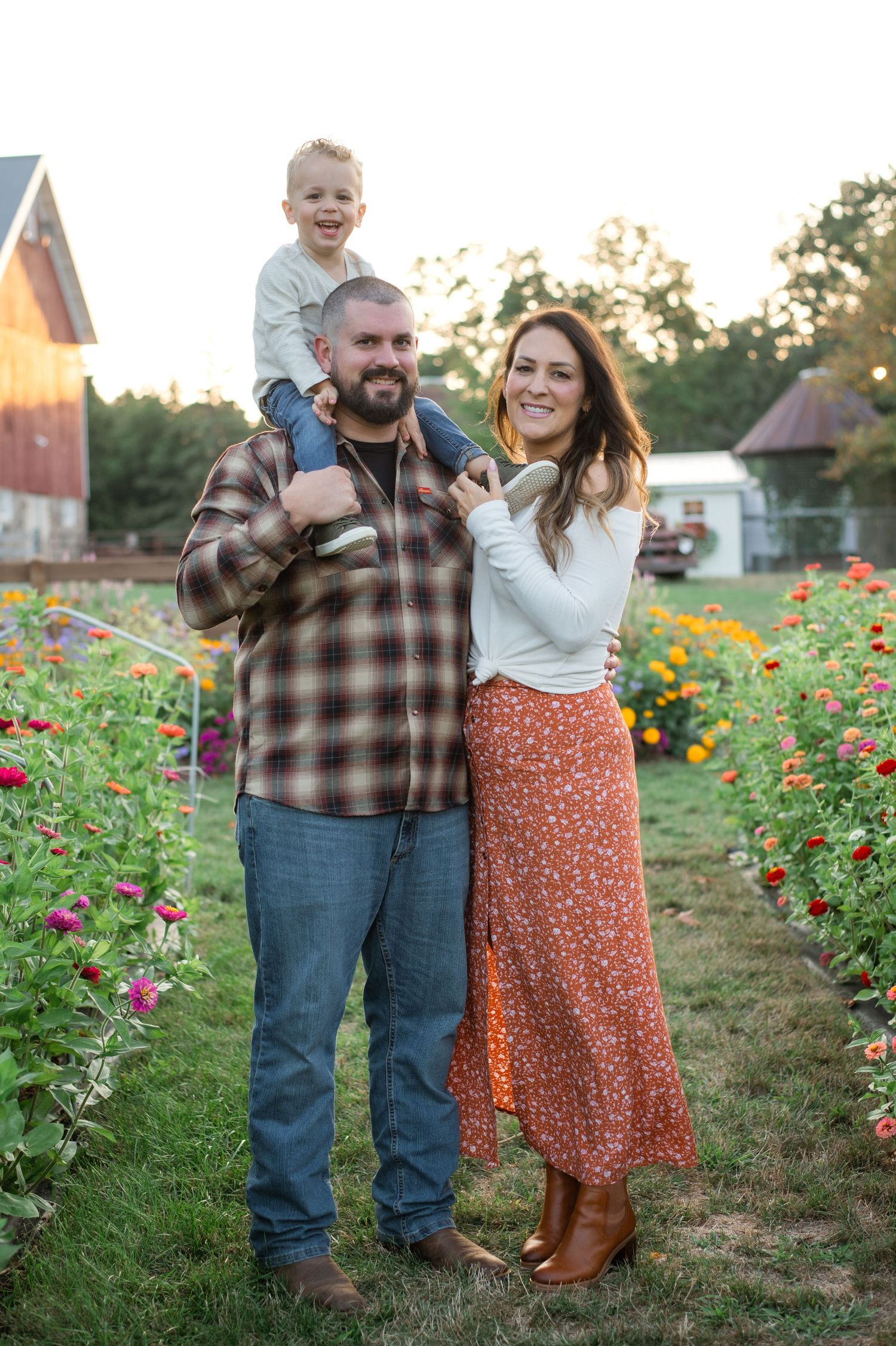 A cheerful family poses together in a garden path lined with vibrant flowers during golden hour.
