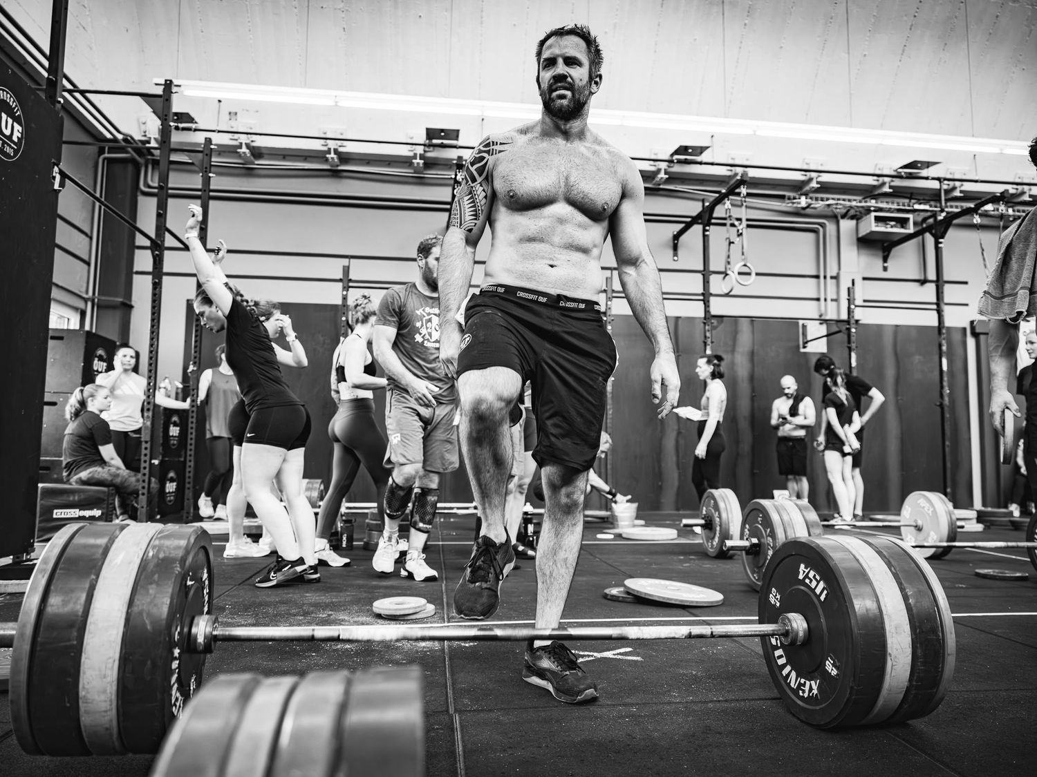 Athletes performing barbell lifts during an intense CrossFit workout in a gym setting.