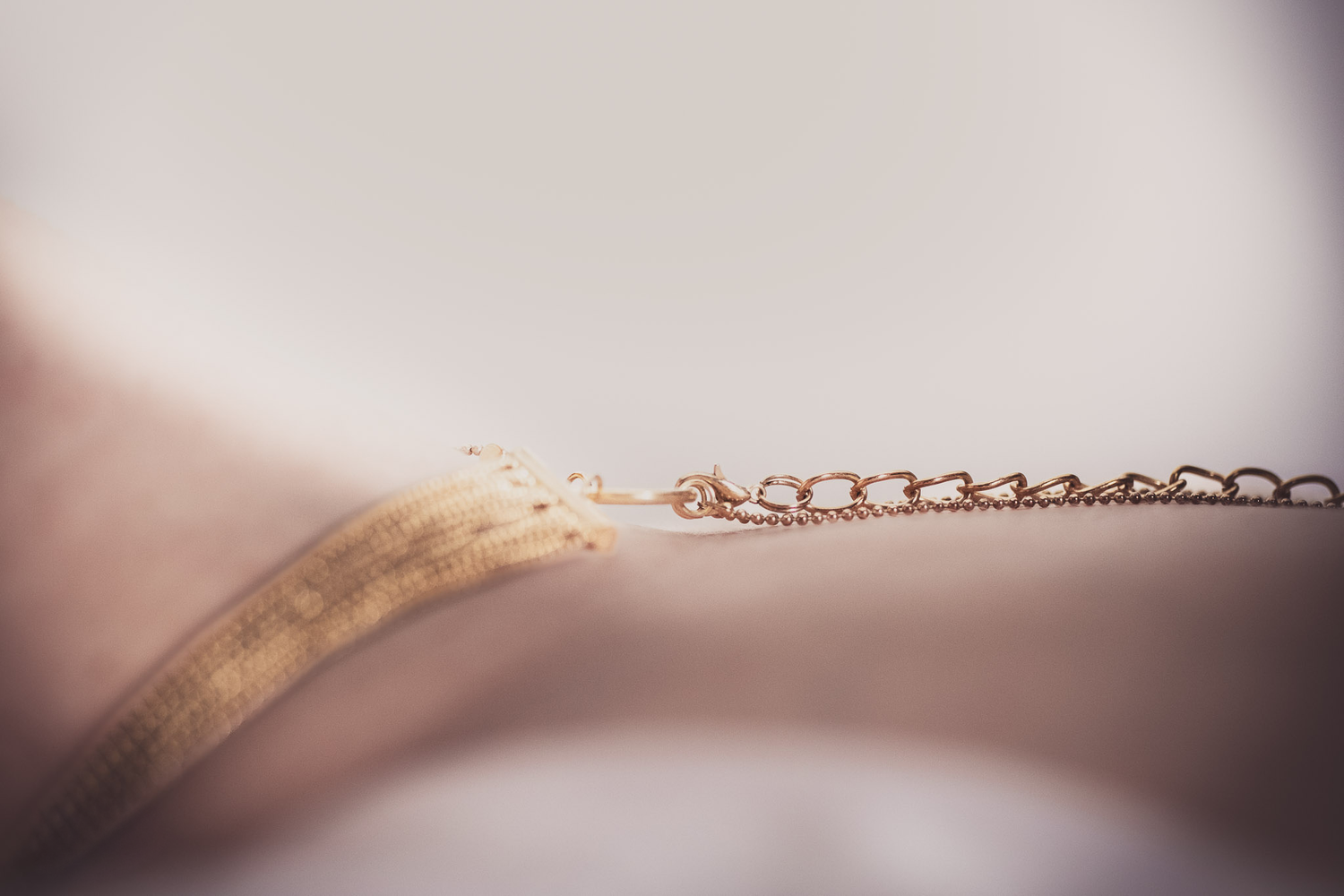 Delicate rose gold chain necklace on soft pink background with shallow depth of field.