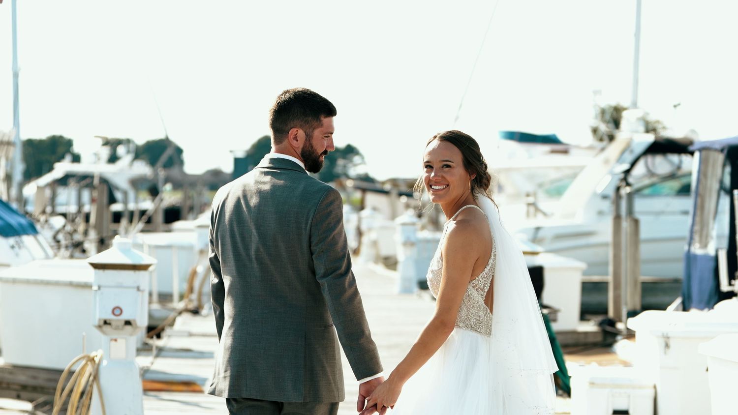 A romantic wedding couple shares an intimate kiss while sitting on a boat at a marina on their special day.