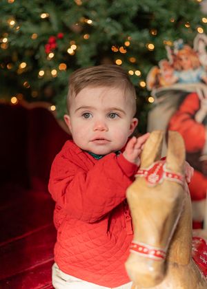 A child in a red sweater touches decorative holiday items near a lit Christmas tree.