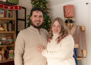 A couple poses for a holiday portrait in front of a decorated Christmas tree and bookshelf.
