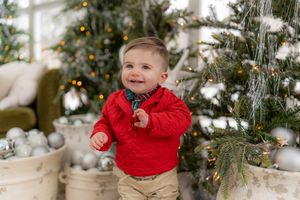 A joyful toddler in red plays with Christmas decorations near a decorated tree.