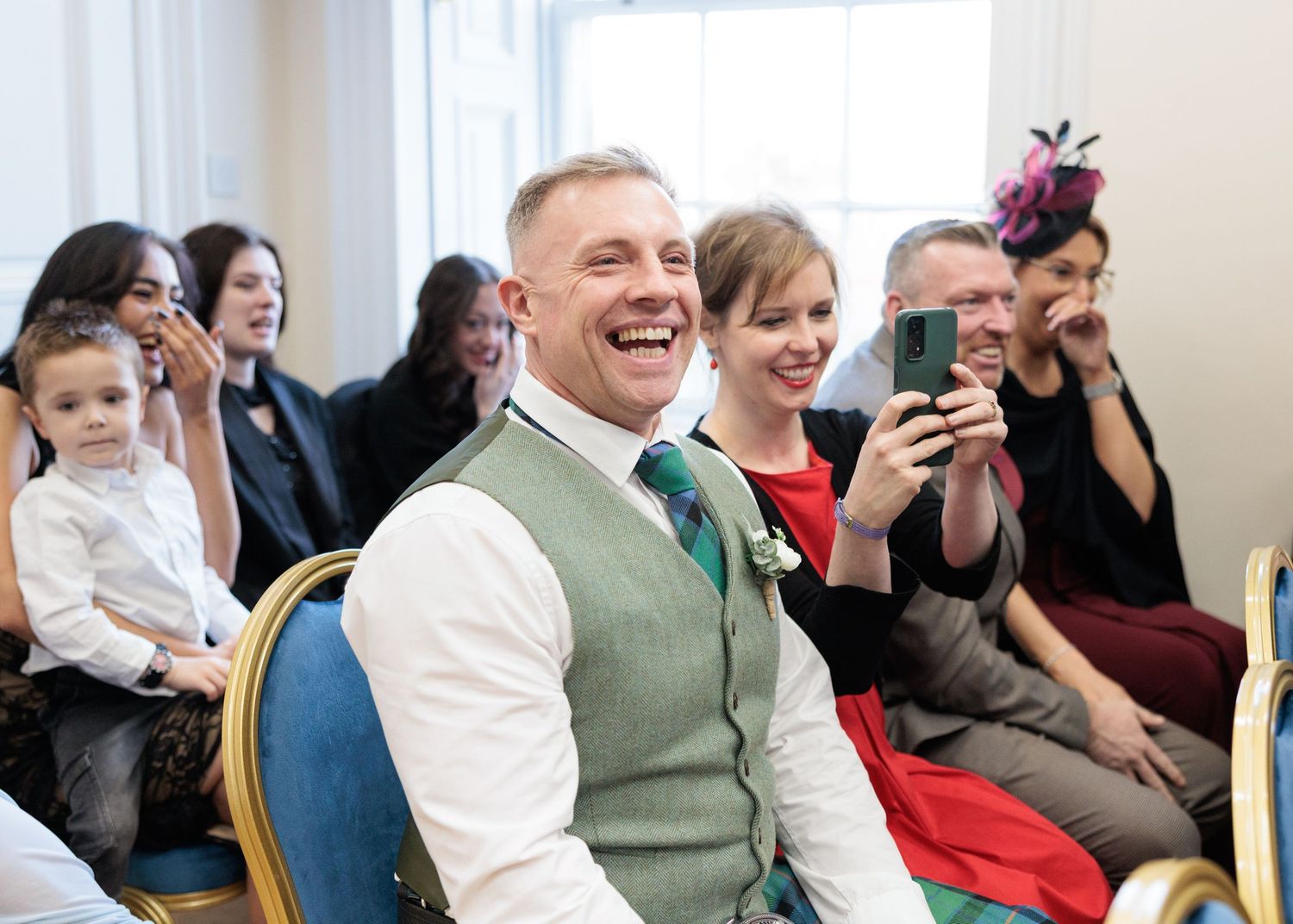 Wedding guests laughing and smiling while seated in rows during a celebration.