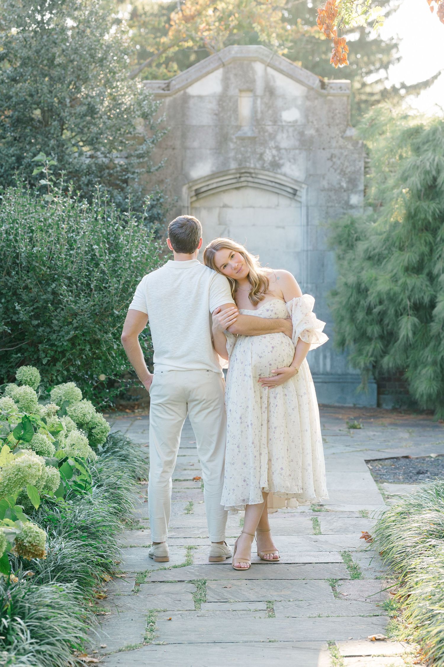 Family in white outfits walking together along a garden path with lush greenery and stone walls.