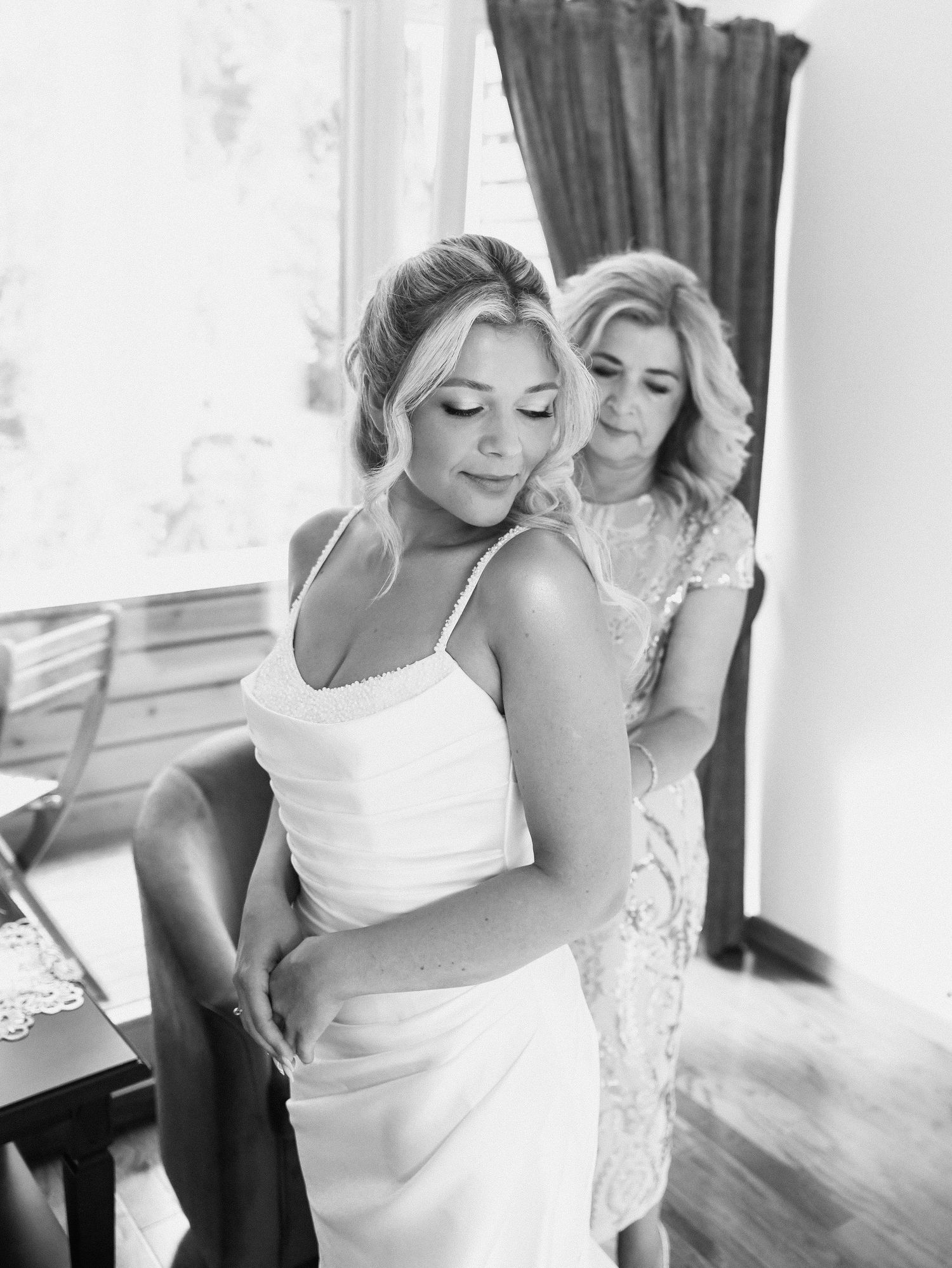 Black and white photo series showing intimate moments of a bride getting ready with help from loved ones on her wedding day.
