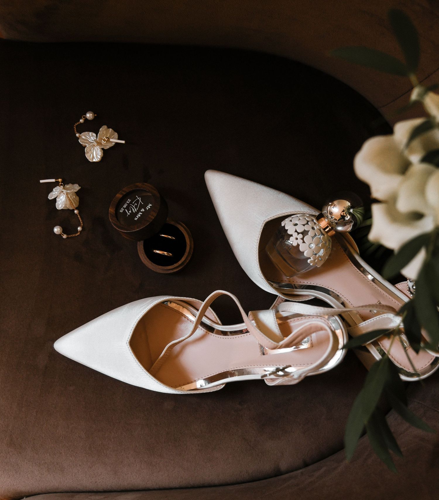 A collection of white bridal shoes and wedding rings arranged artistically on a dark brown surface.