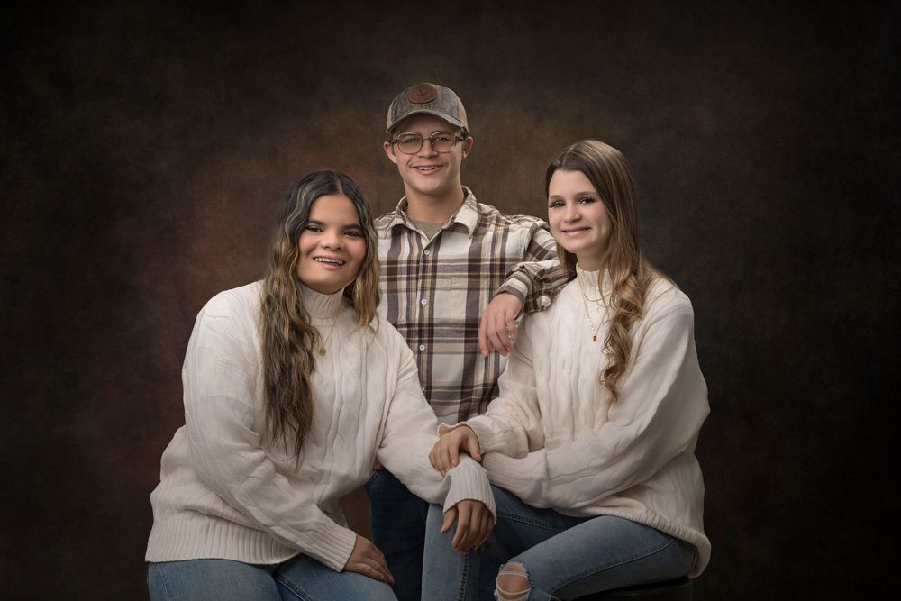 A family portrait showing siblings in coordinated cream and brown outfits against a dark background.