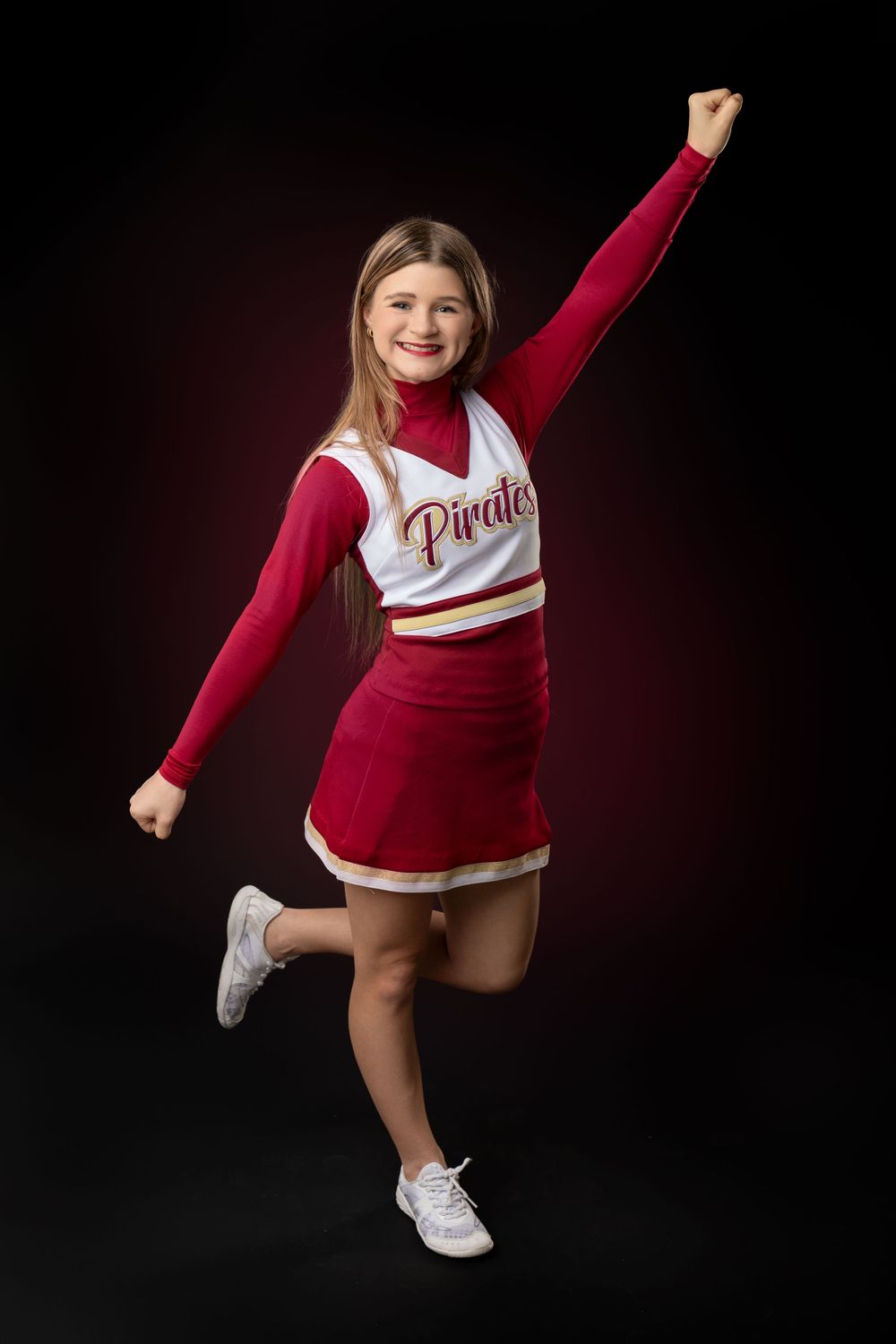 A cheerleader in red and white uniform jumps energetically against a dark background.