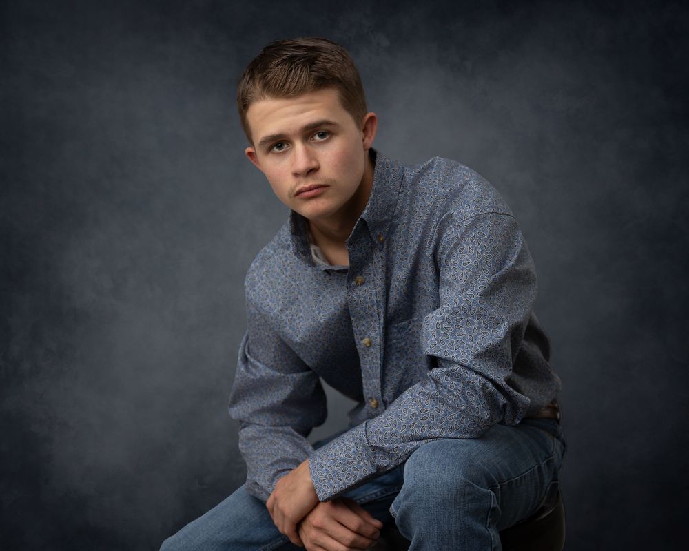 Studio senior portrait session with dark dramatic lighting and casual blue attire.
