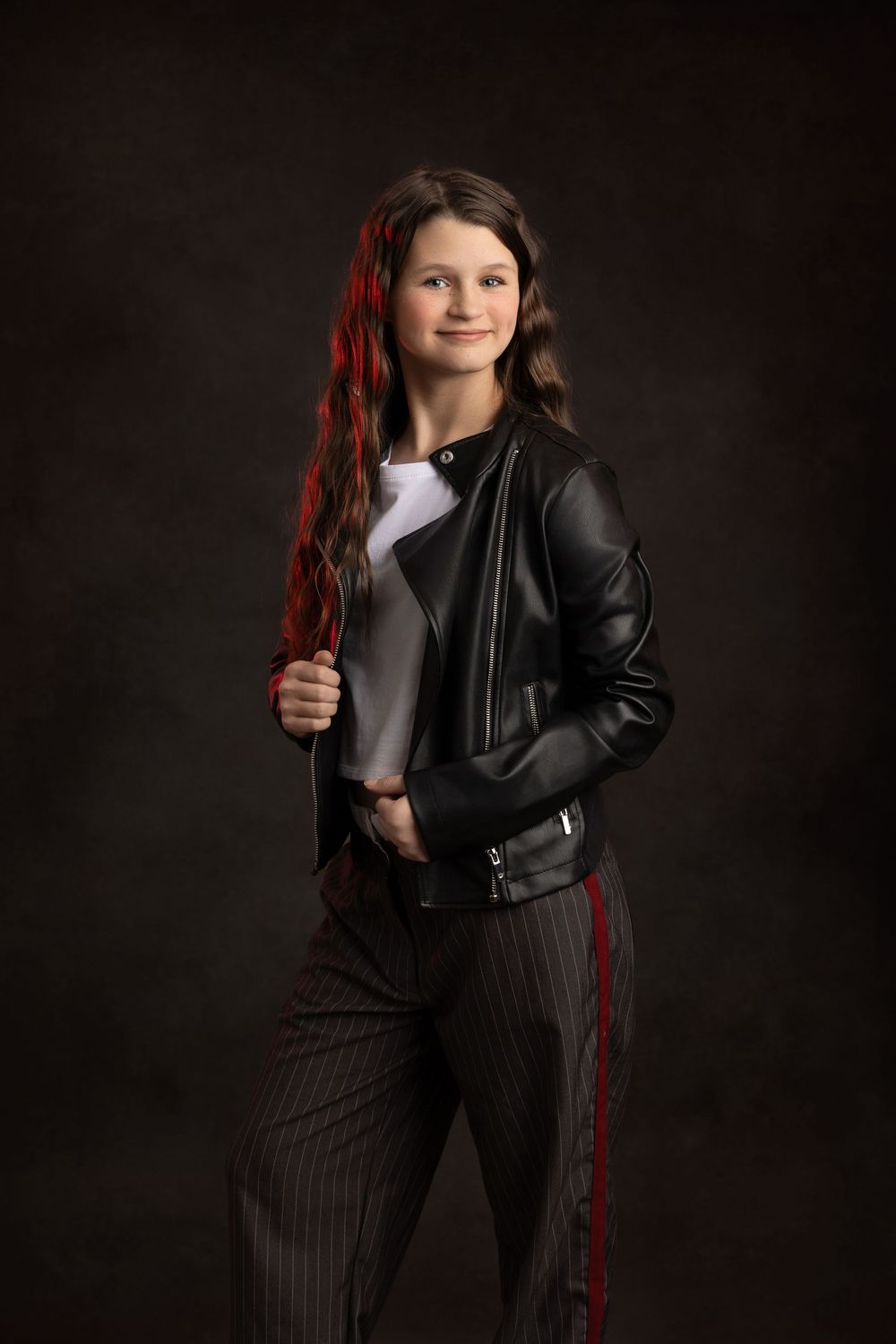 A stylish leather jacket and pinstriped pants create an edgy portrait look against a dark backdrop.