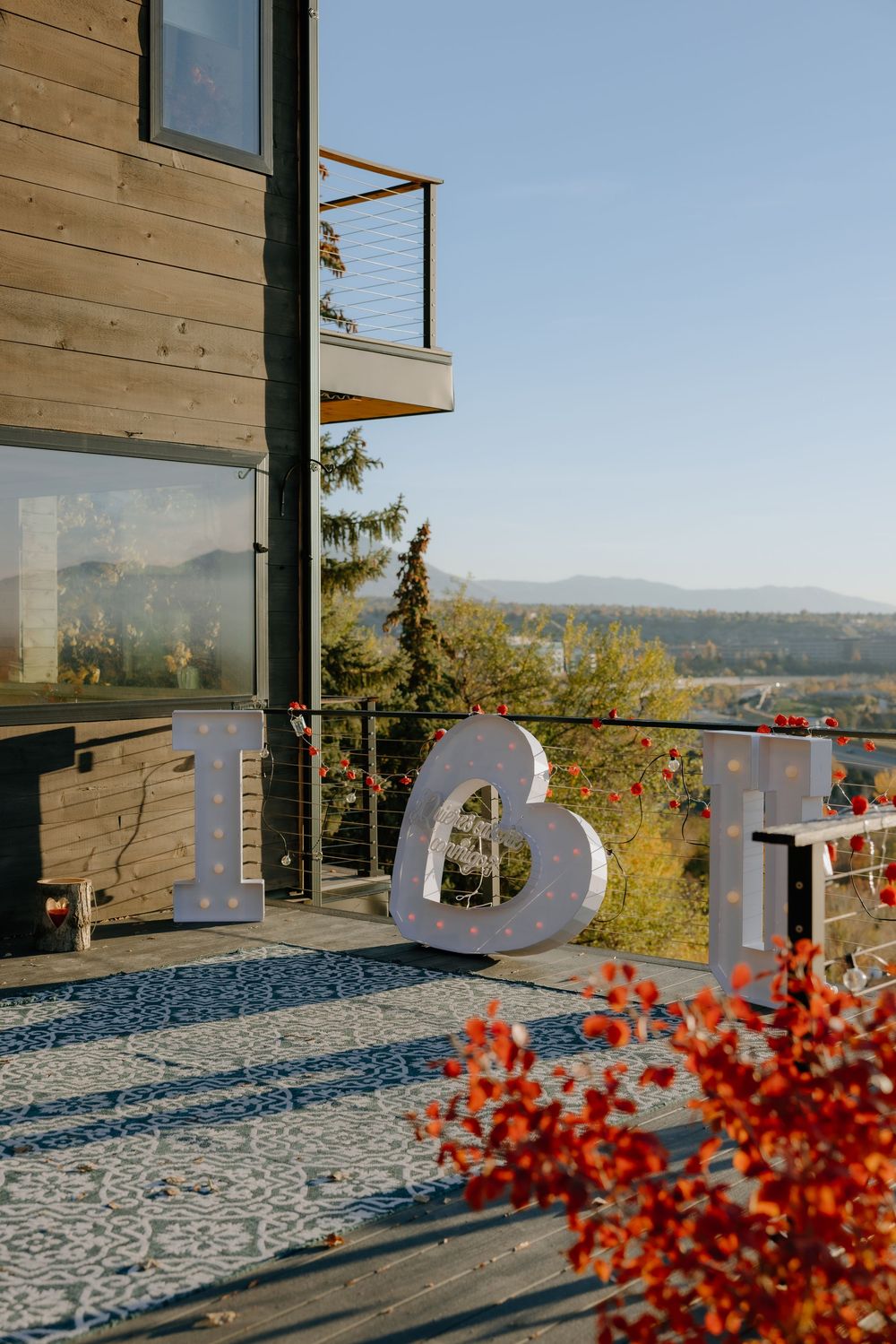 Modern outdoor deck with white sculptural letters and blue tile flooring against a scenic mountain backdrop in autumn.