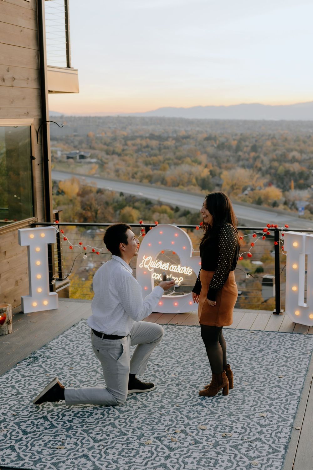 A romantic proposal scene unfolds on a scenic balcony overlooking an autumn landscape at sunset.