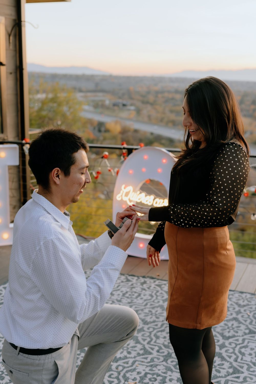 A romantic proposal moment captured at sunset on a scenic balcony with mountains in the background.