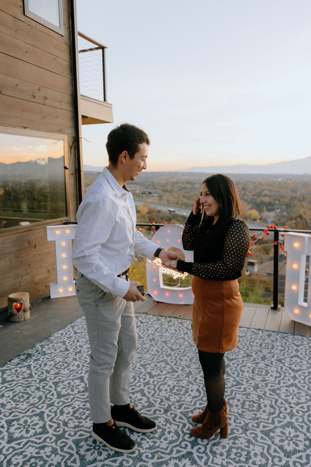 Two people dance together on a patterned deck with string lights and a scenic mountain view at sunset.