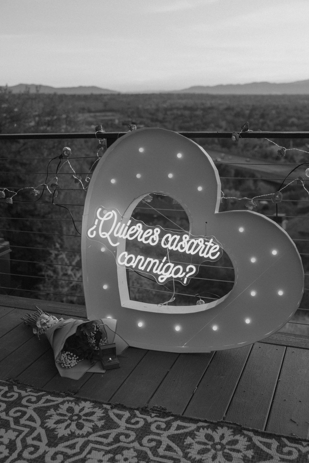 Black and white sequence showing illuminated LED text sign being assembled on a rooftop with mountains in background.