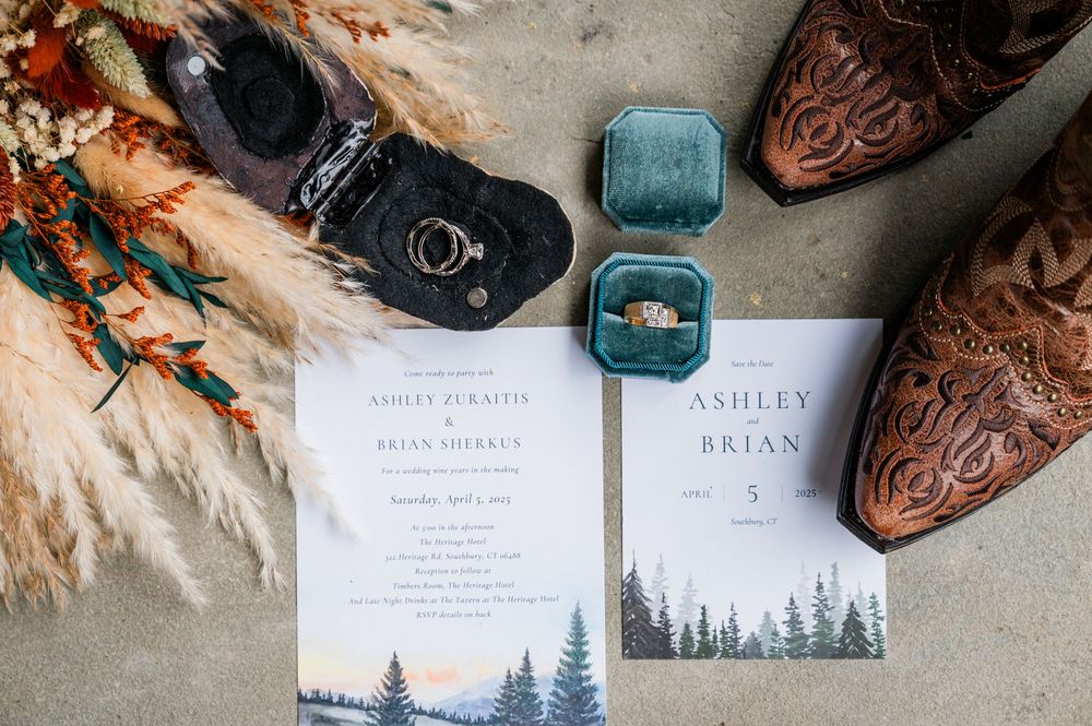 Wedding invitations with forest scenery alongside cowboy boots and a turquoise ring box.