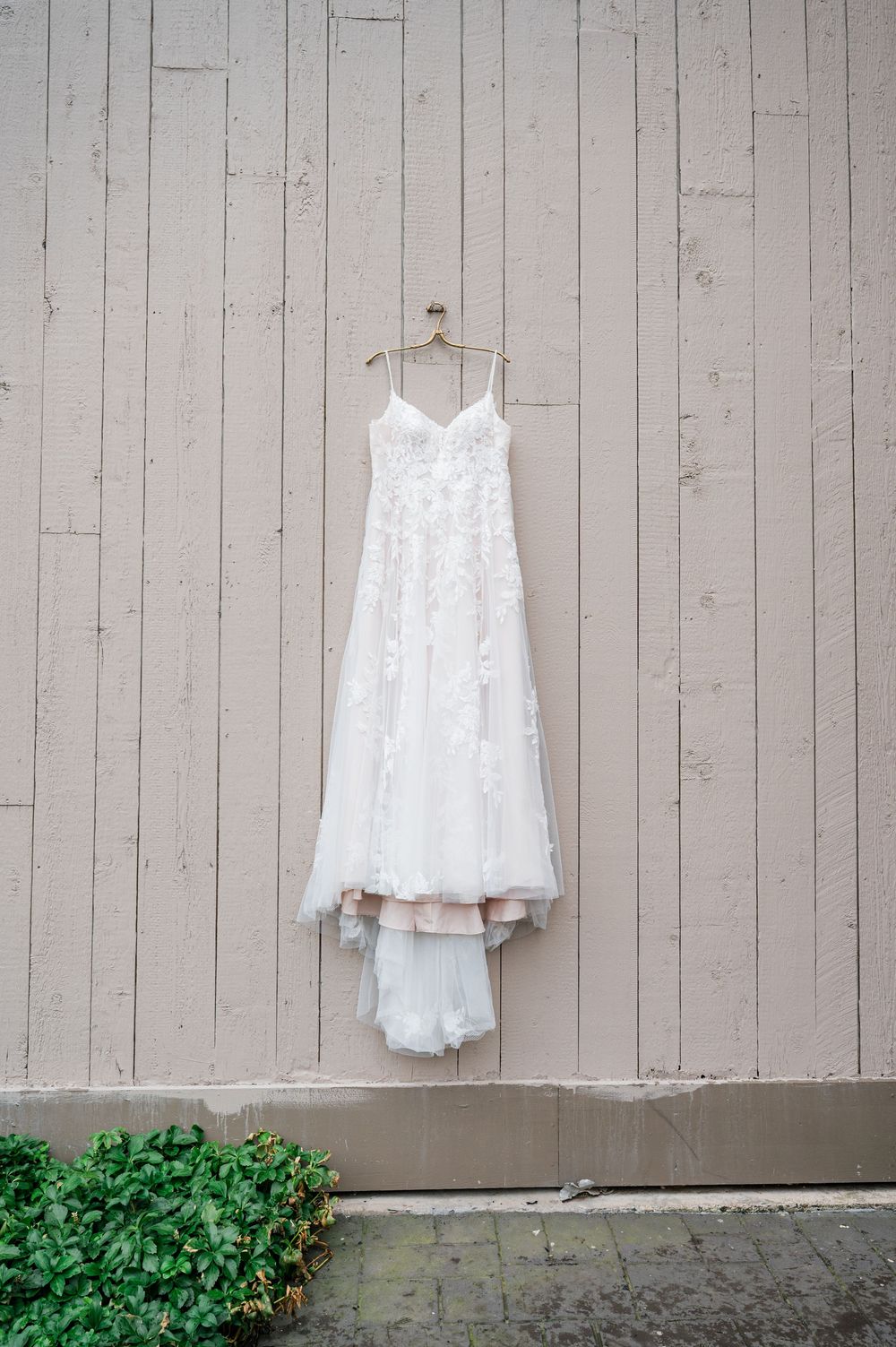 White wedding dresses hanging on beige wooden wall for detail shot.