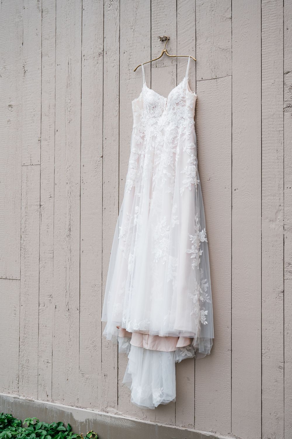 White lace flower girl dresses hanging on rustic wooden wall for wedding day preparation.