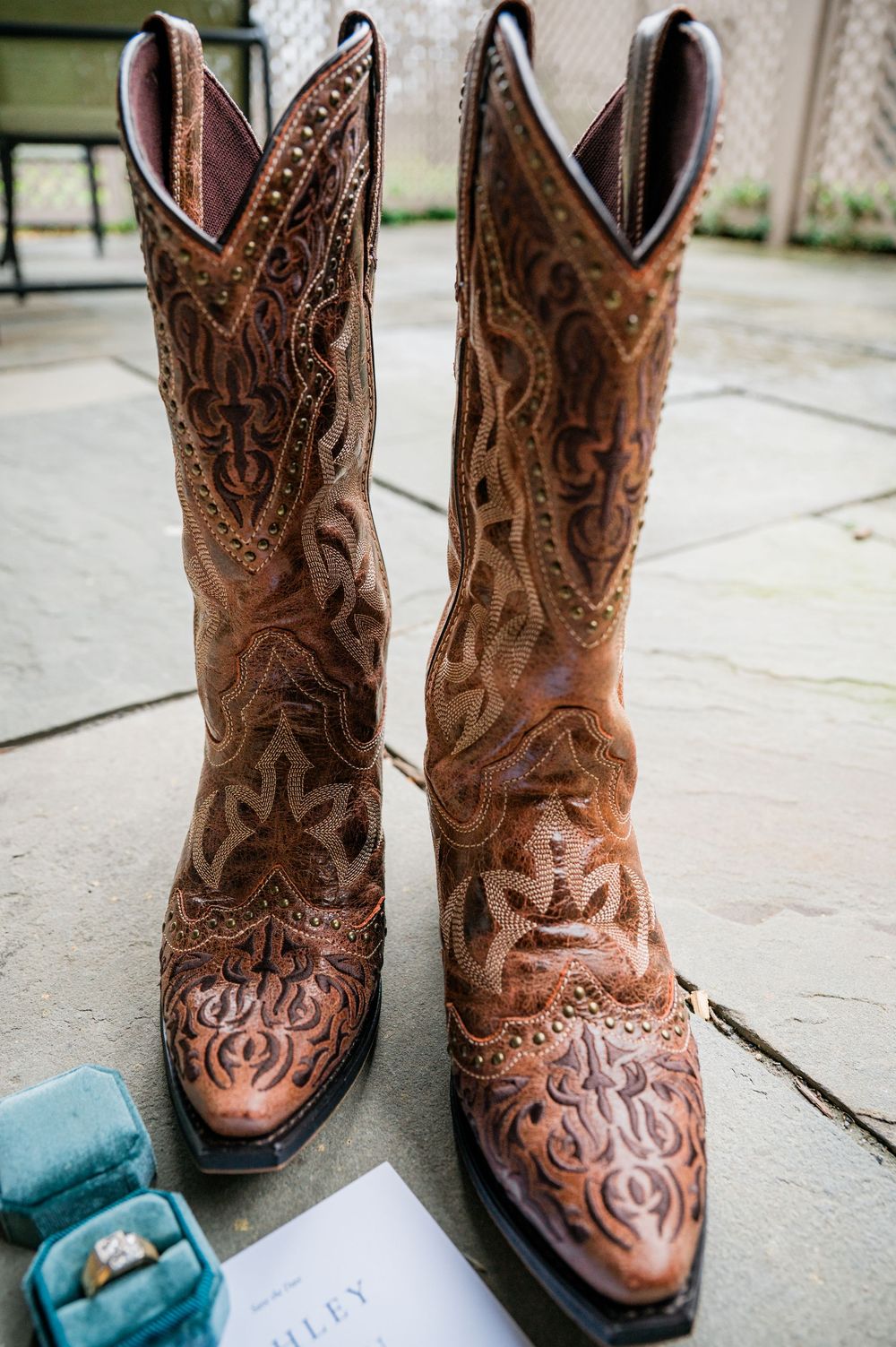 Detailed brown leather cowboy boots with intricate embroidery patterns displayed on wooden floor.