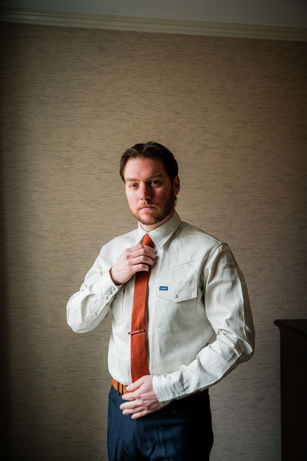 Man in white dress shirt and orange tie poses in a series of artistic portraits against a textured wall.