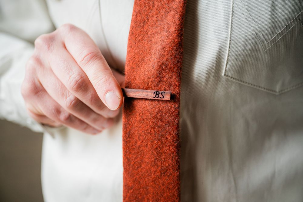 Close-up detail of a tie clip on an orange necktie against a white shirt.