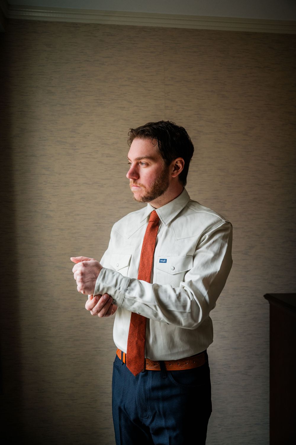 Groom adjusts cuffs while getting ready in formal attire with orange tie.