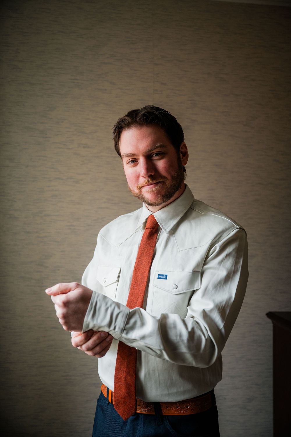 Person adjusting white dress shirt and orange tie against neutral grey background.