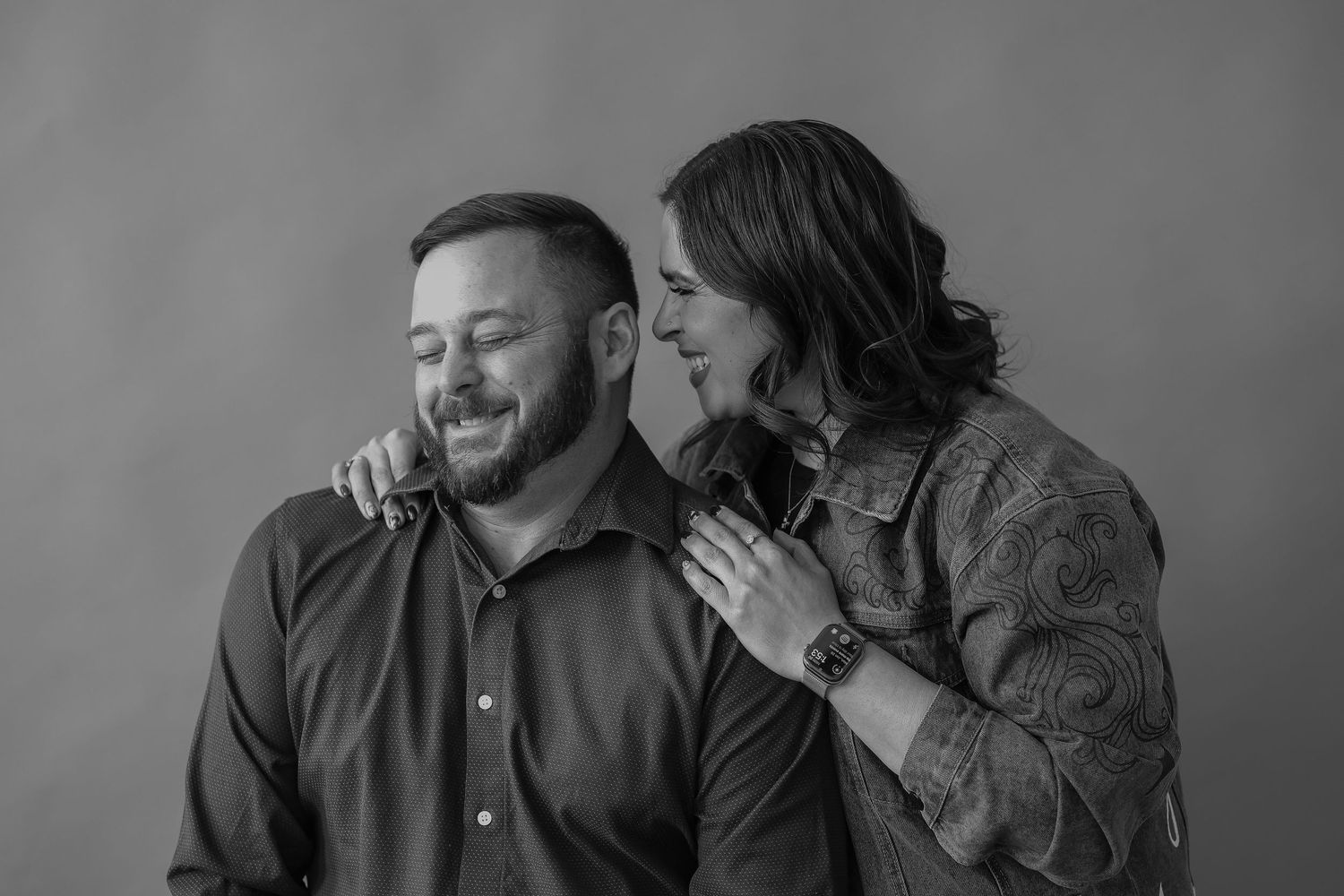 A black and white intimate portrait of a couple sharing a candid laughing moment together.
