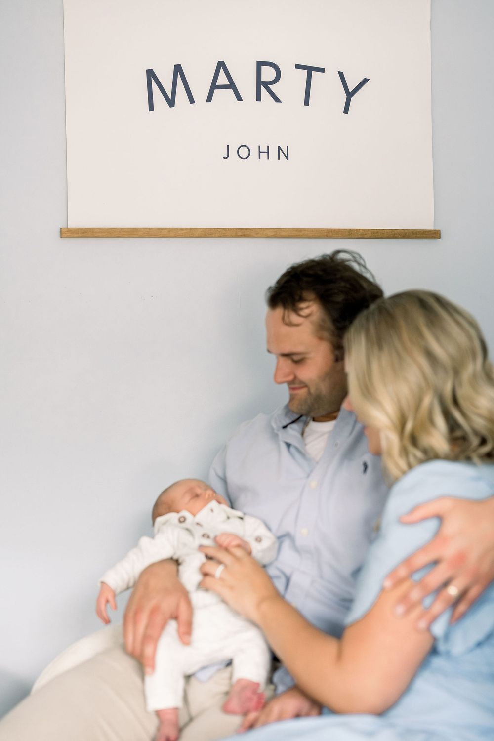 Parents hold their newborn baby in a hospital room with a name sign reading 'Marty' displayed on the wall.